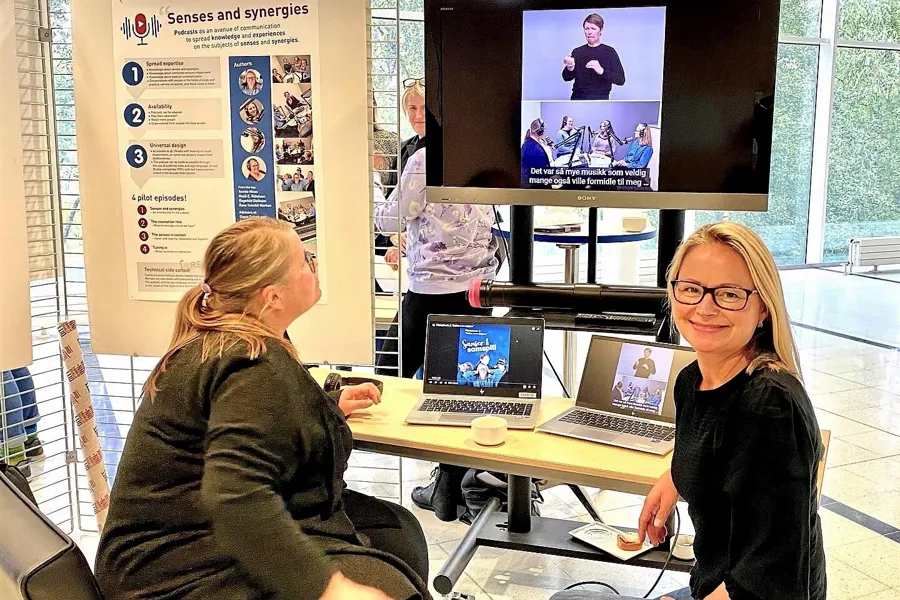 Kvinner sitter ved et bord med bærbare datamaskiner og en projektorskjerm