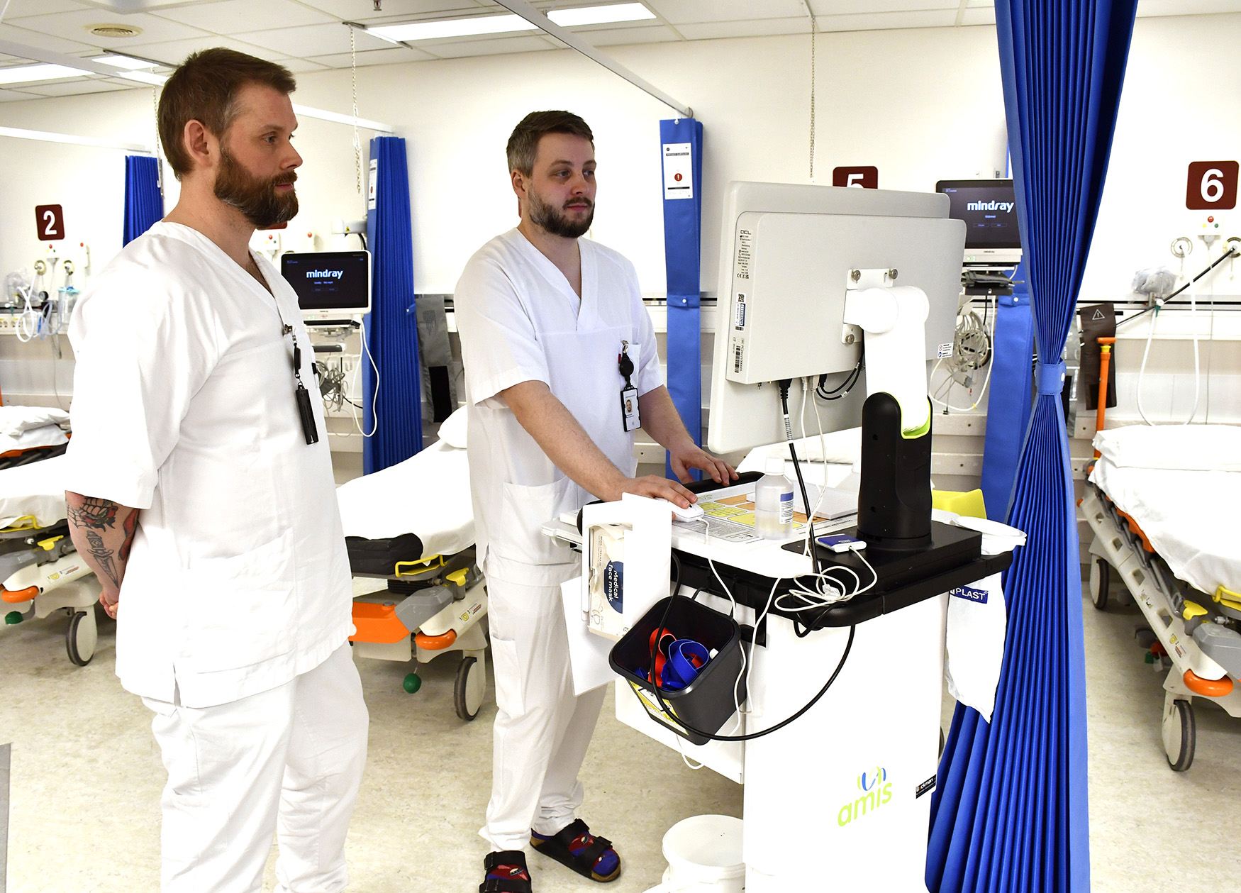 Et par menn i hvite laboratoriefrakker i et rom med bord og blå gardin