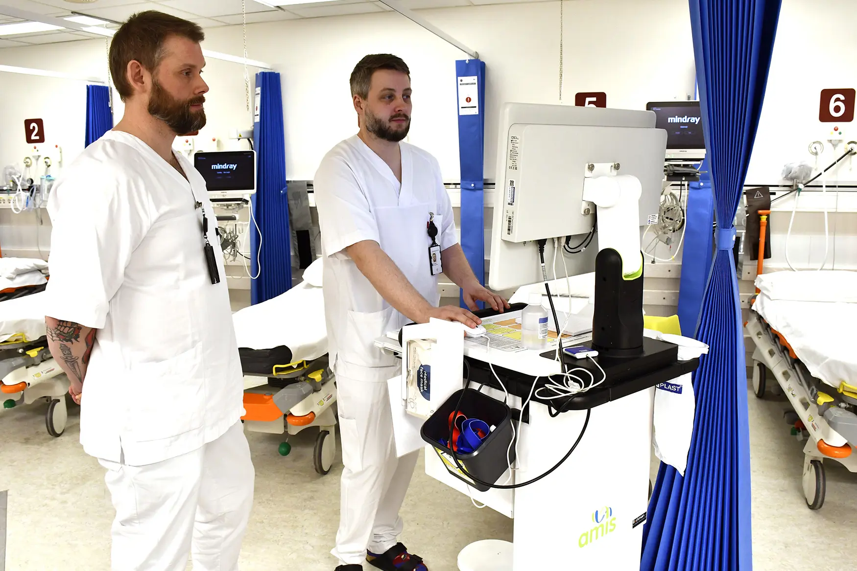 Et par menn i hvite laboratoriefrakker i et rom med bord og blå gardin