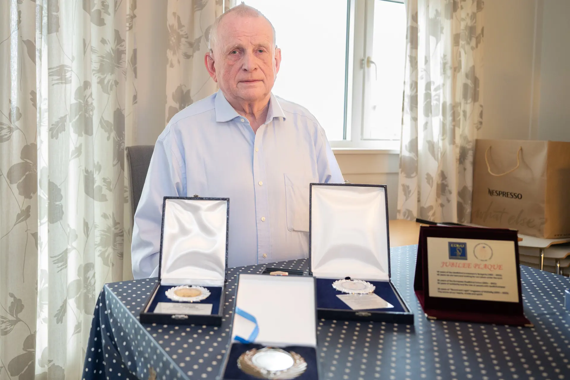 En mann som sitter ved et bord med flere medaljer og diplomer