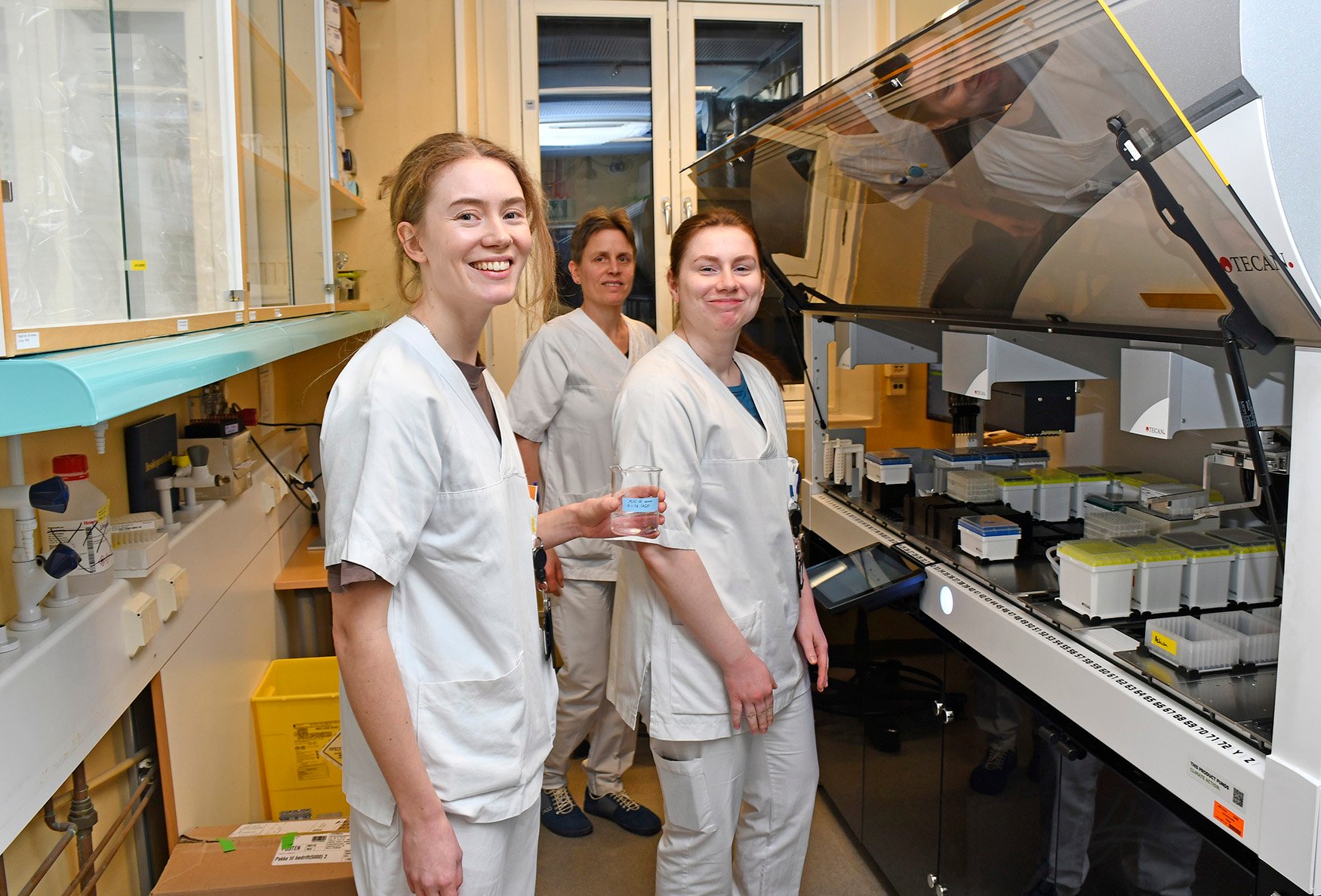 En gruppe kvinner i hvite laboratoriefrakker står foran en maskin