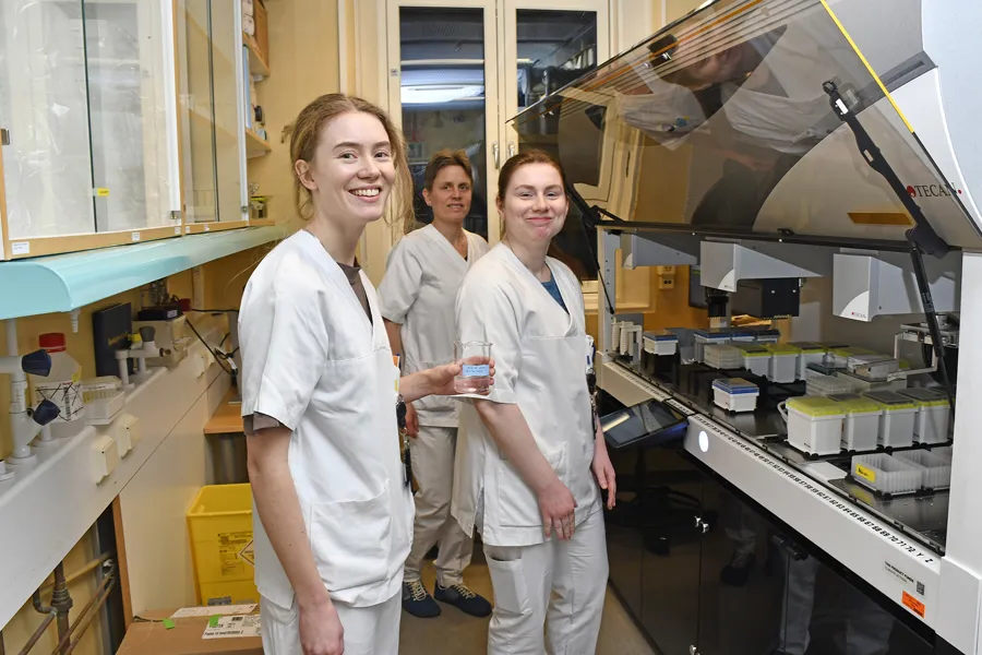 En gruppe kvinner i hvite laboratoriefrakker står foran en maskin