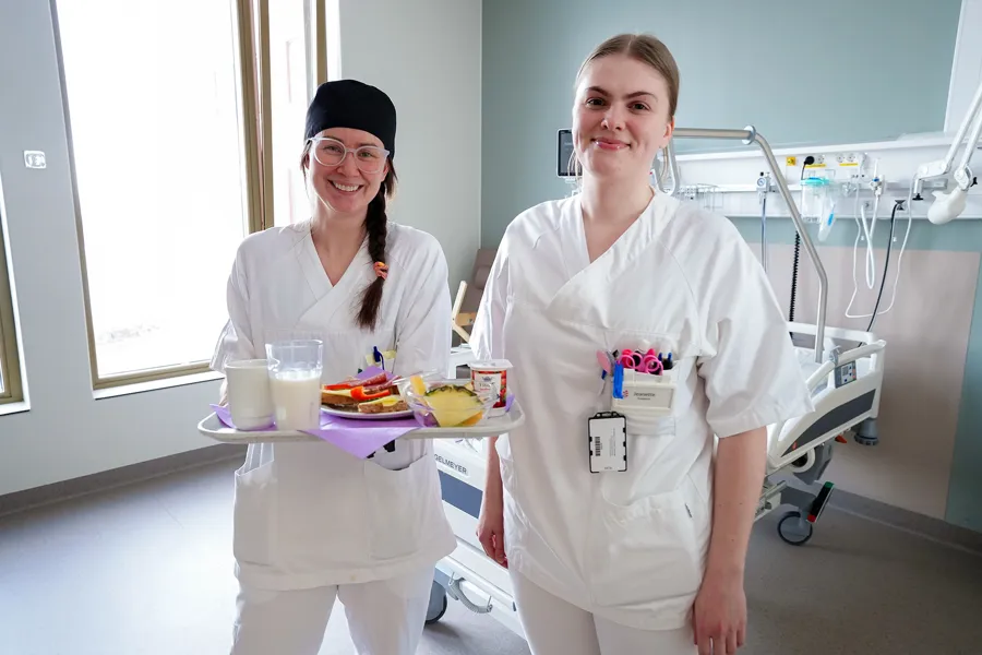 Et par kvinner i hvite frakker som holder mat og smiler