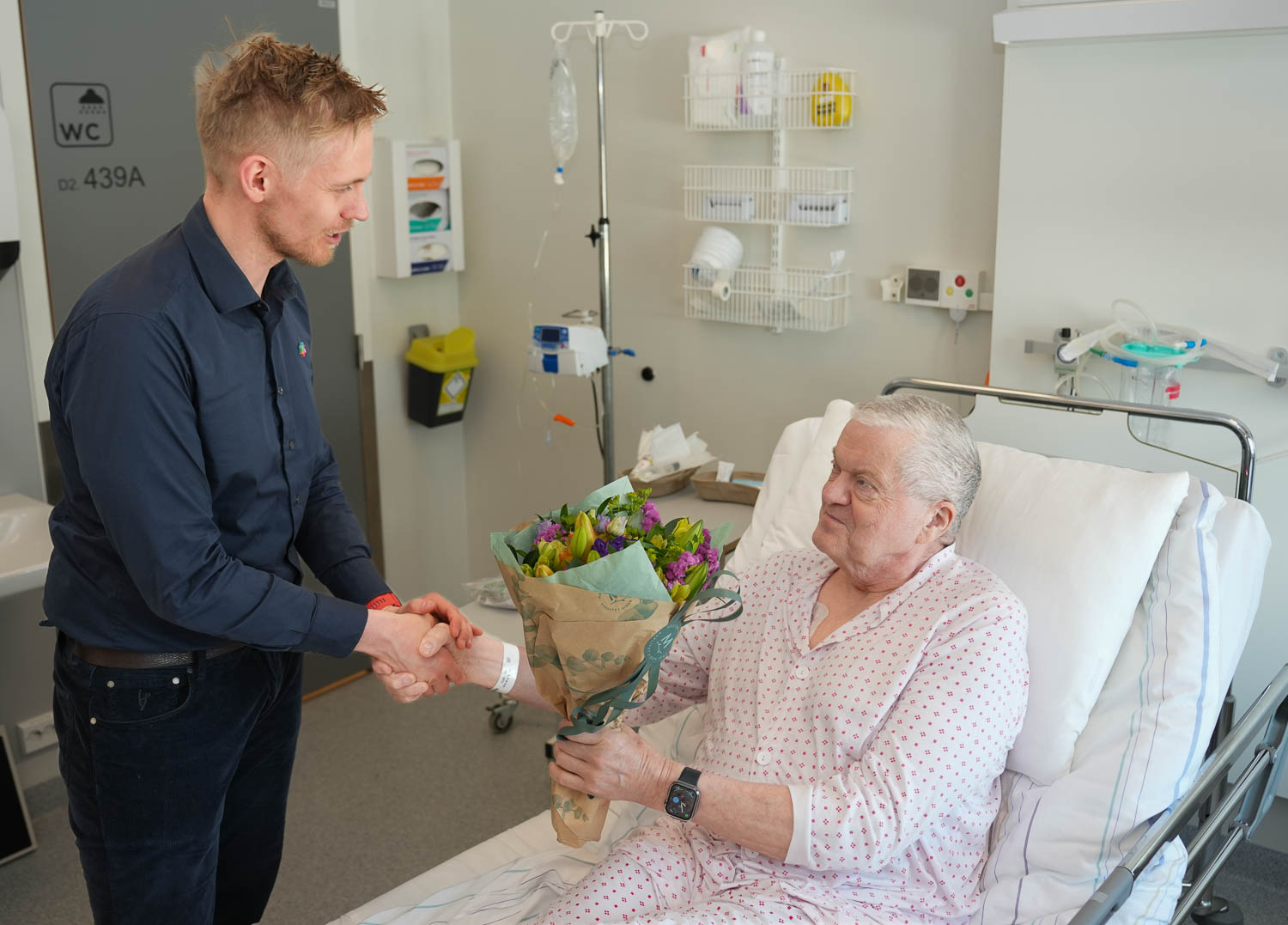 En mann i en sykehusseng som blir undersøkt av en lege