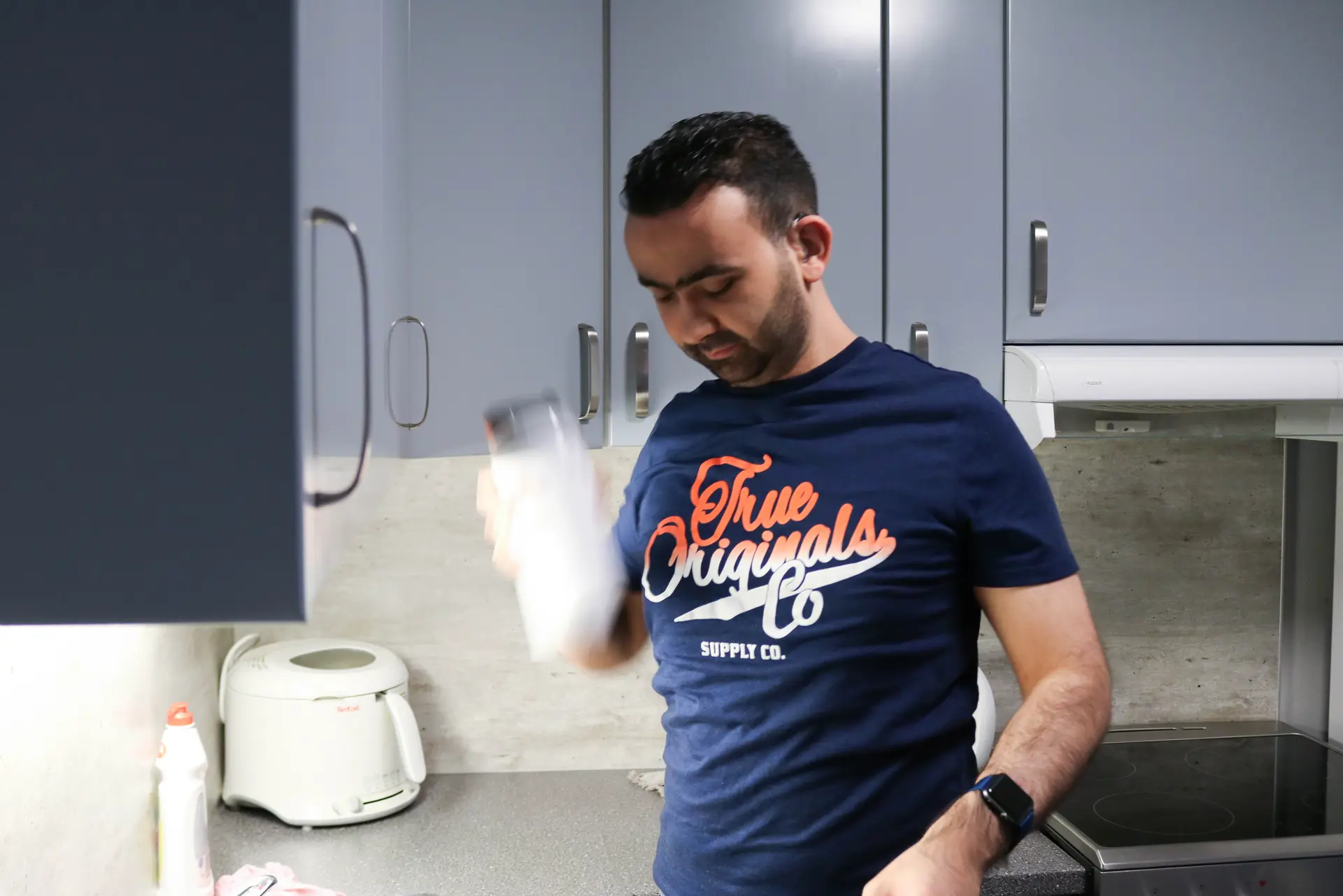 Døvblind mann står på sitt kjøkken og rister en drikkeflaske med proteinpulver