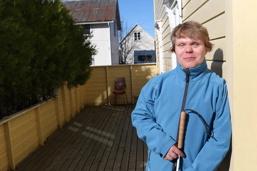 En mann som holder en gåstav og lener seg mot en husvegg