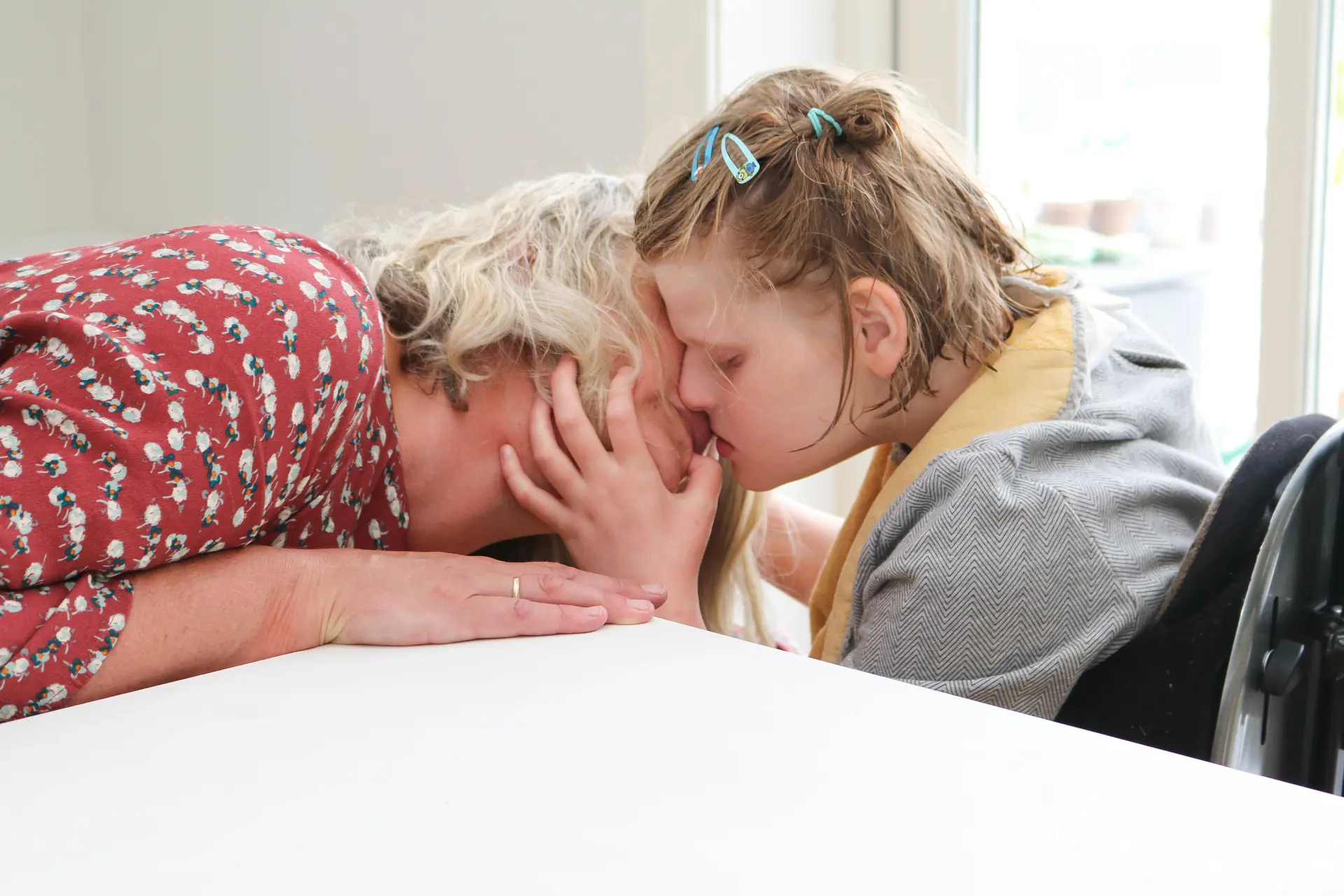 Mor og datter helt tett, hodet mot hodet. Datter klemmer sin venstre hånd rundt morens hake, hals og kinn.