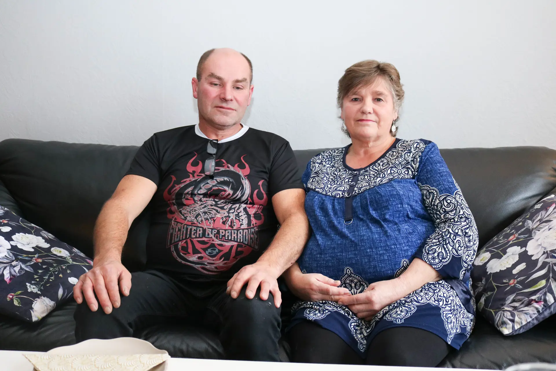 Ektepar, han i svart t-skjort og hun i blå kjole, sitter sammen i grå skinnsofa