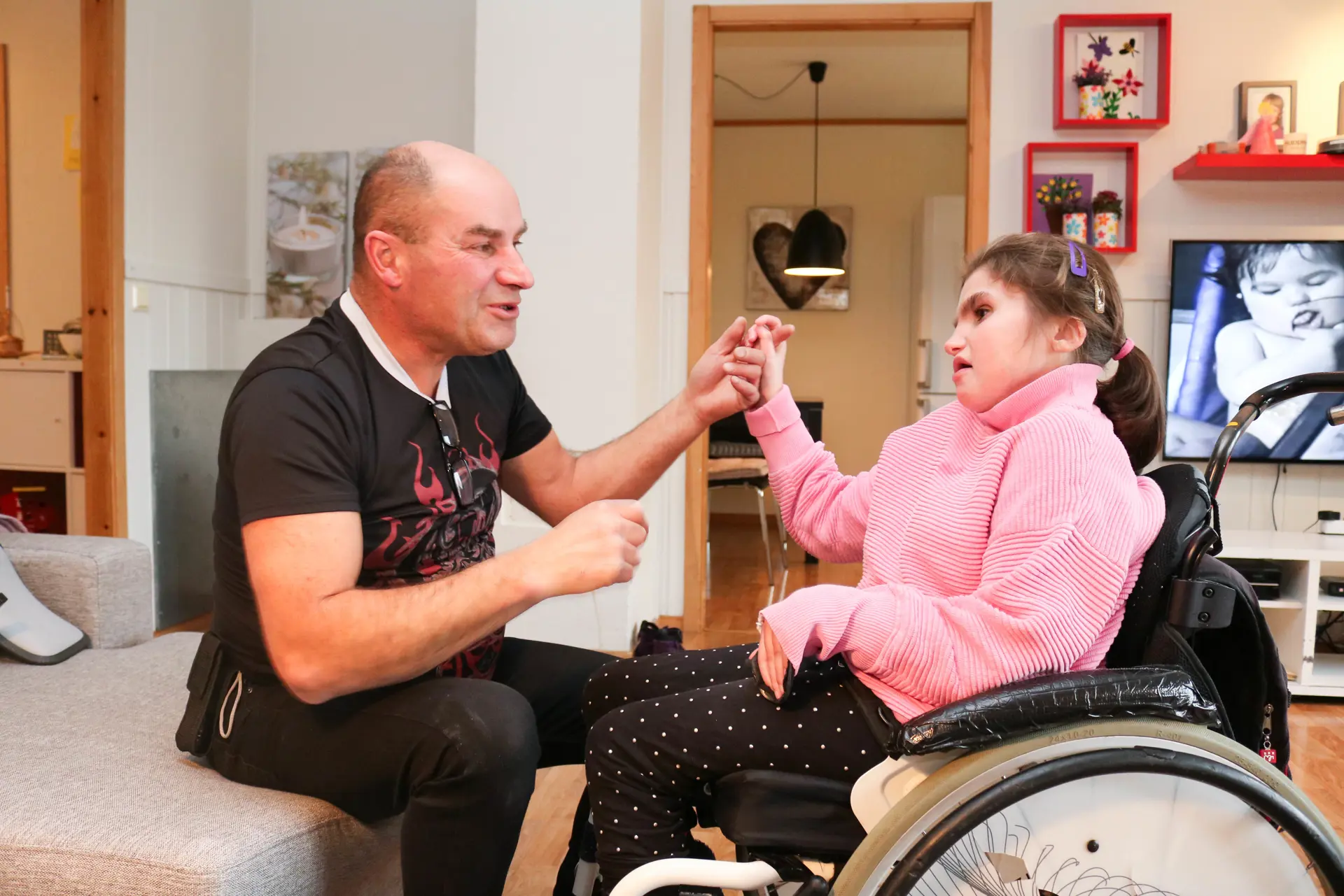 Far kommuniserer med tegnspråk sammen med sin datter. Hun sitter i rullestol og de er hjemme i hennes egen stue.