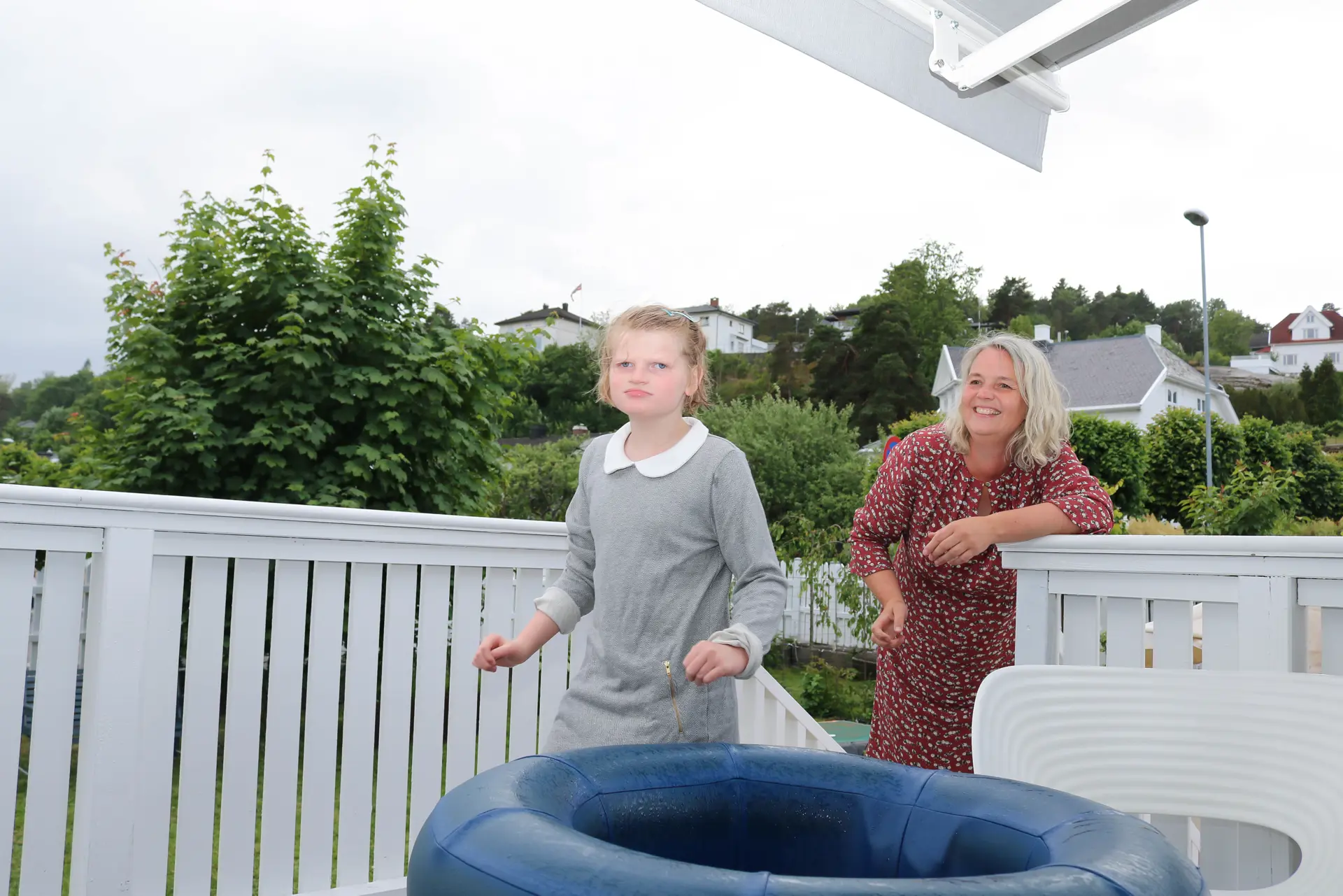 Mor og datter på hvitmalt terrasse. Datter nærmest ved en blå badering