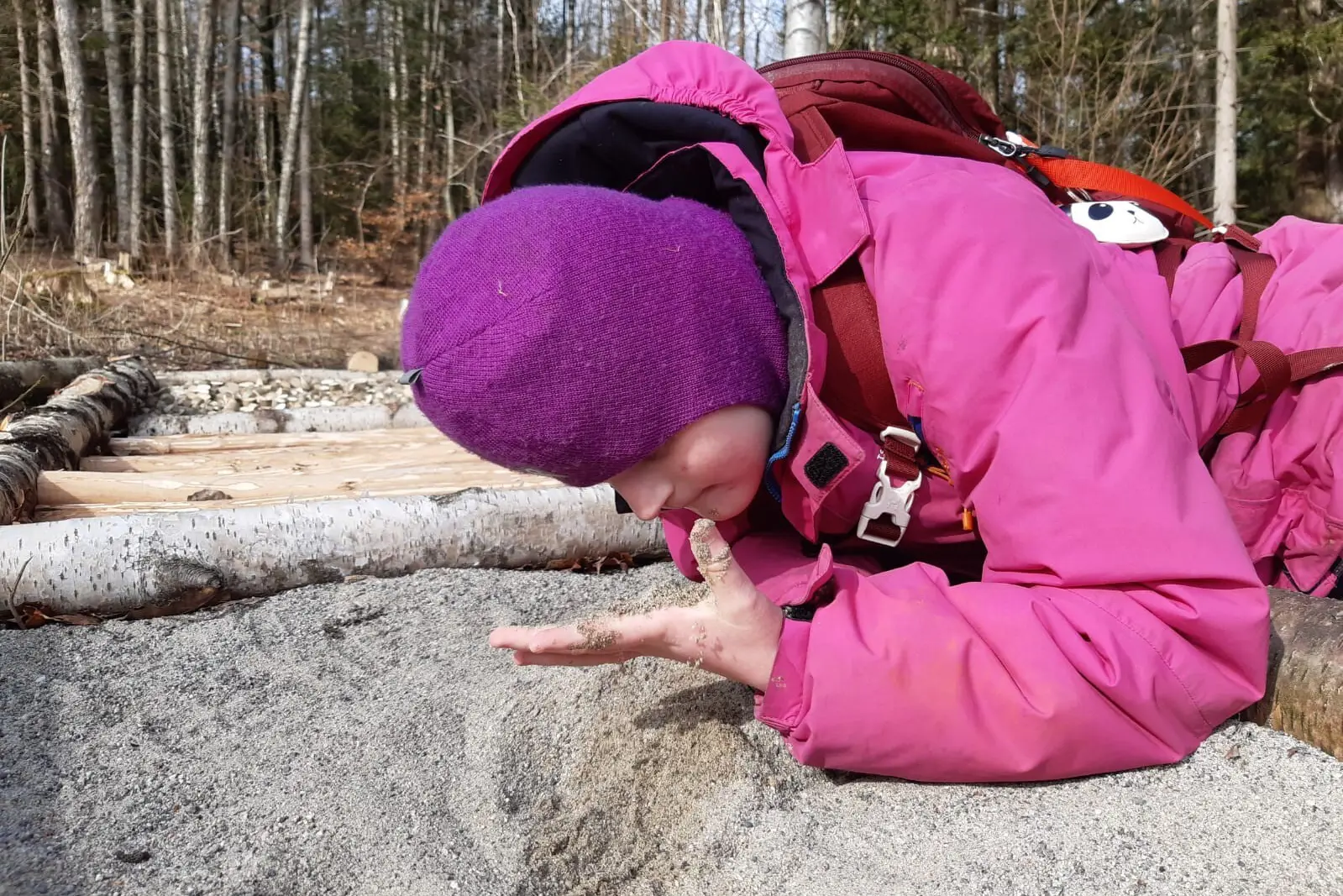Jente i rosa jakke ligger i en sandgrop