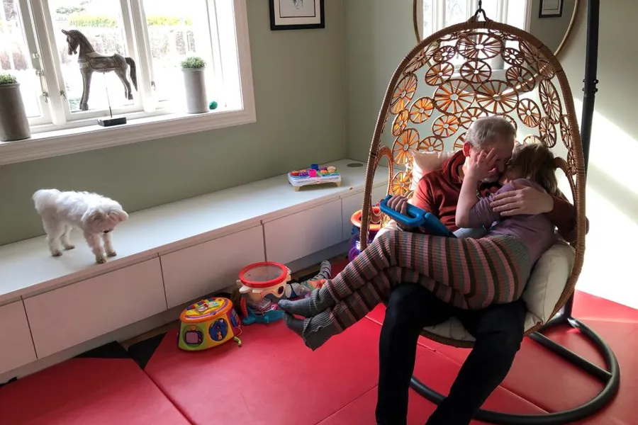 Jente med medfødt døvblindhet sitter i fanget på sin far i en hengestol