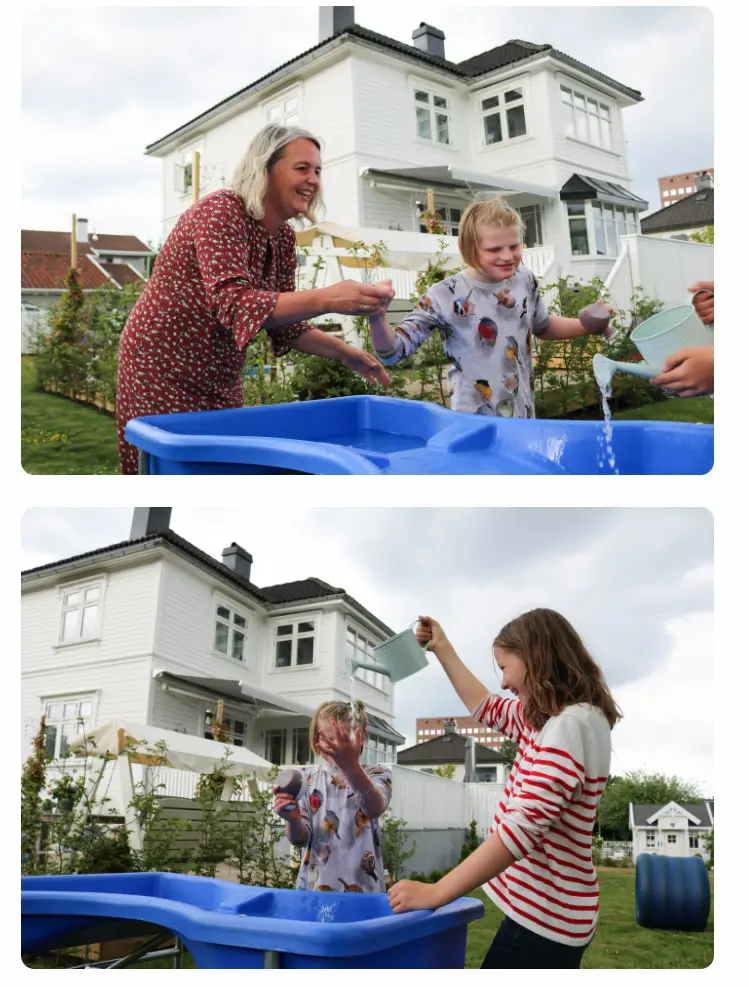 Mor og datter leker ved et fuglebad i en sommerhage. Hvit trevilla i bakgrunnen