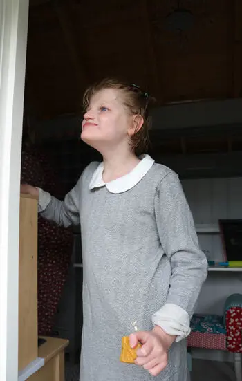 Jente i grå kjole står i en døråpning og ser oppover til venstre