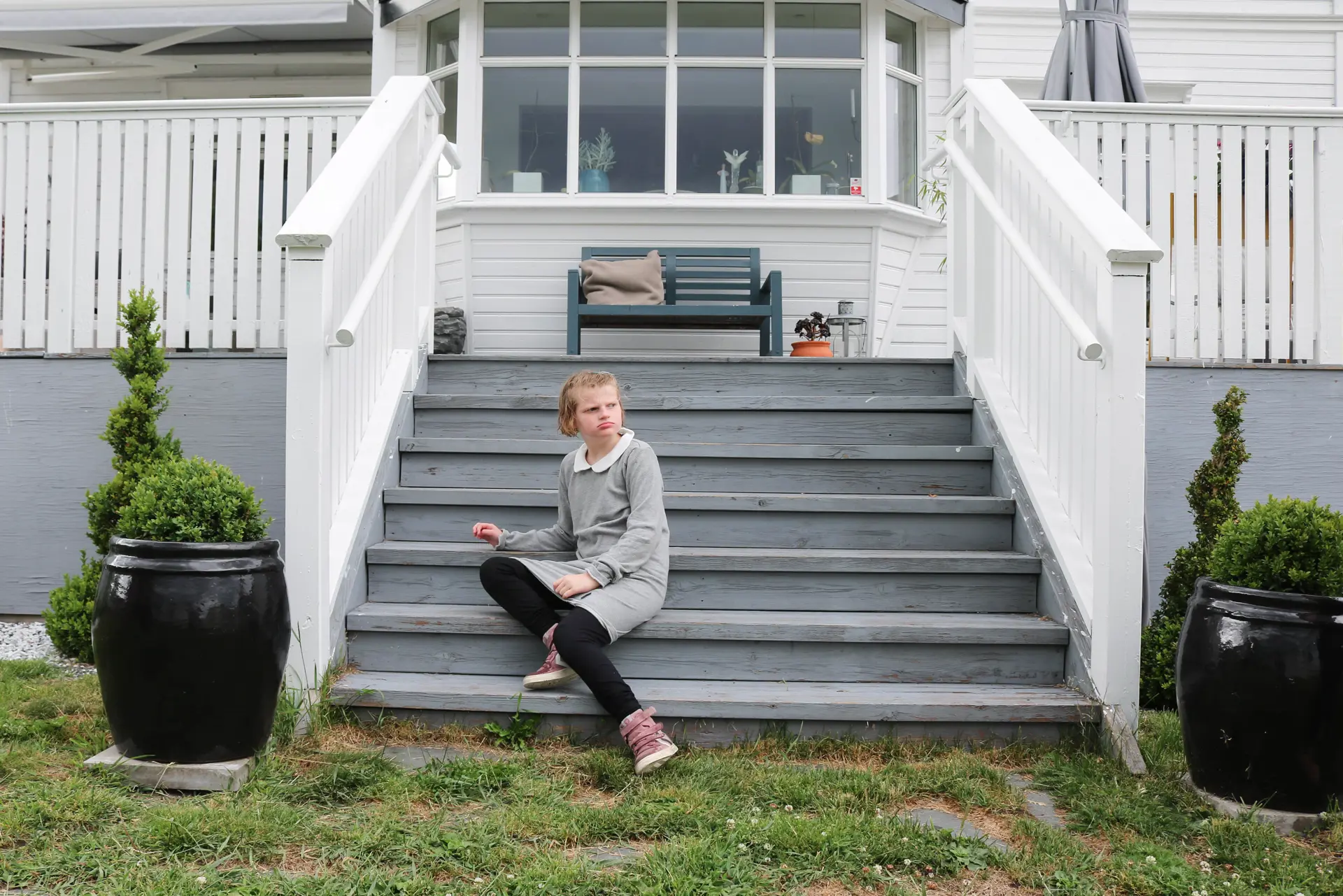 Jente i grå kjole og røde joggesko sitter i en kurvstol på en terrasse