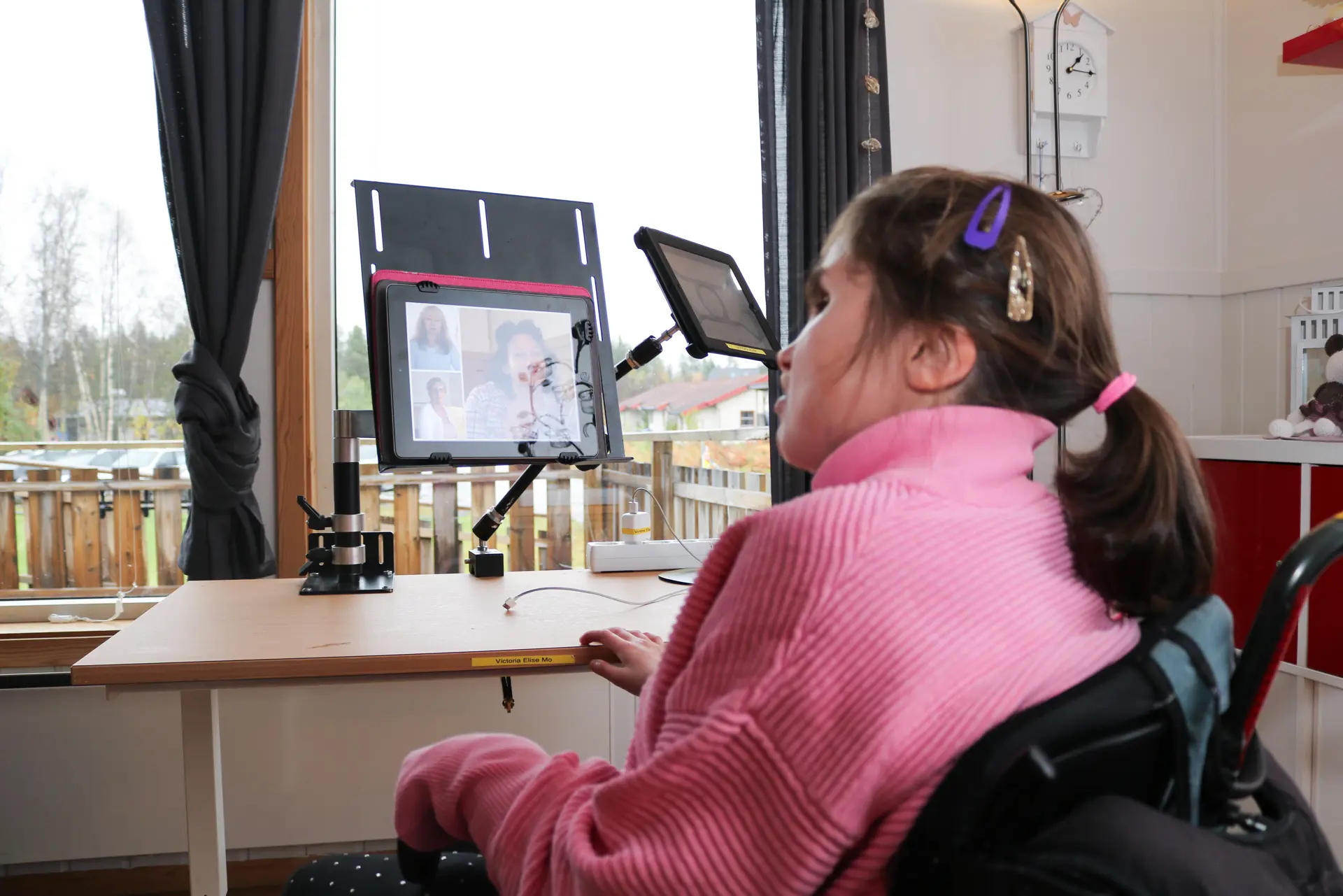 Jente sitter foran Ipadden sin, som er festet til et stativ på et bord.