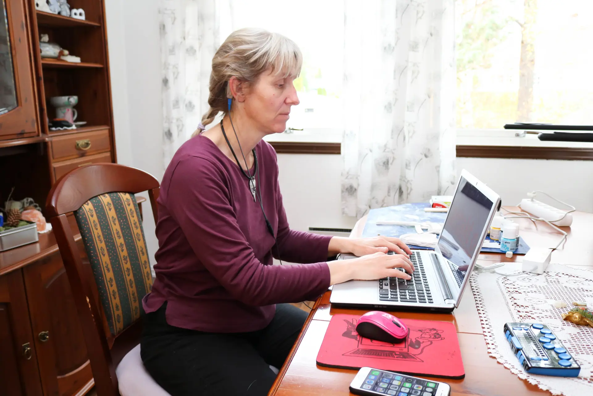 Spisestue. Kvinne i lilla genser sitter ved bordet og skriver på en laptop.