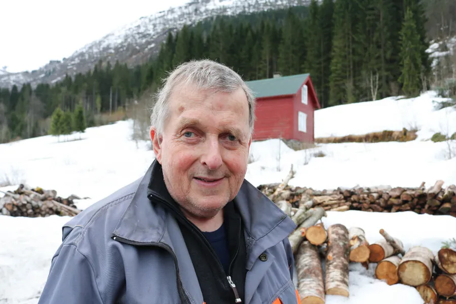 En mann som står i snøen foran noen vedstabler