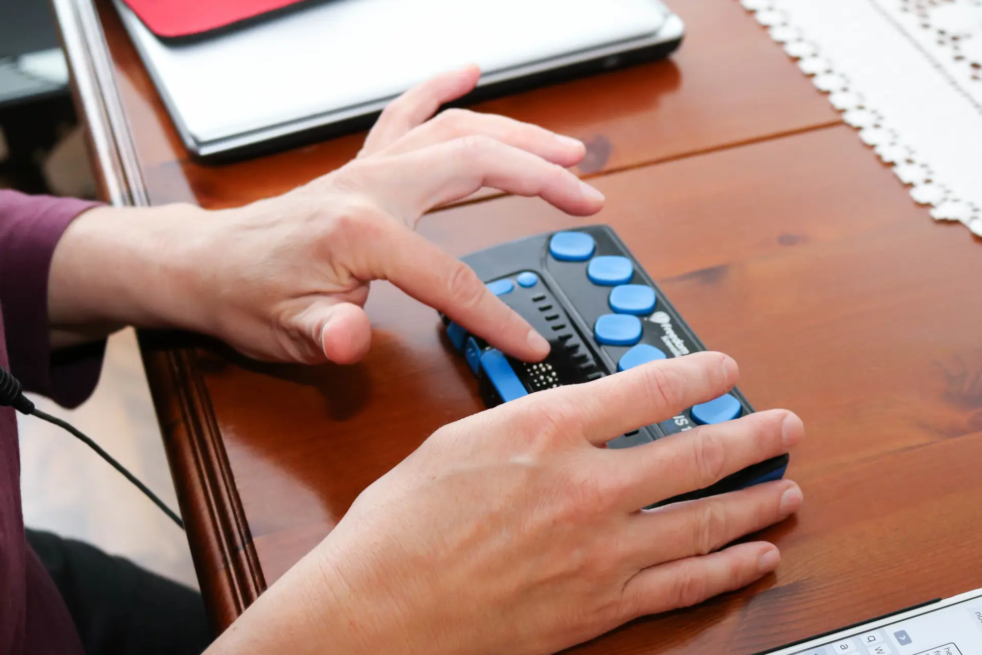 Spisestue. Kvinne i lilla genser sitter ved bordet og taster på blå leselist. Hun hviler hoder på venstre knyttneve.