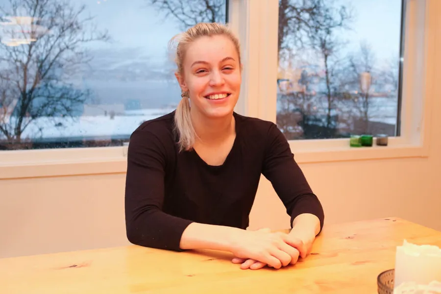 Lyshåret og blid kvinne som sitter med albuene på et bord