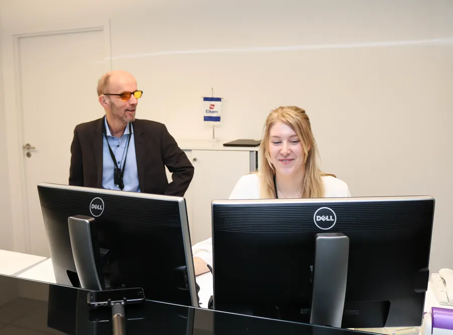 En mann og en kvinne som sitter ved et skrivebord med datamaskiner
