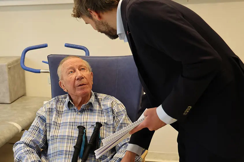 En mann i dress og slips som snakker med en mann i en stol