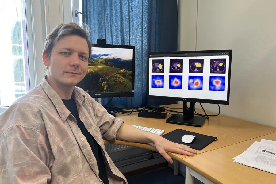 En mann som sitter ved et skrivebord med en datamaskin og en skjerm