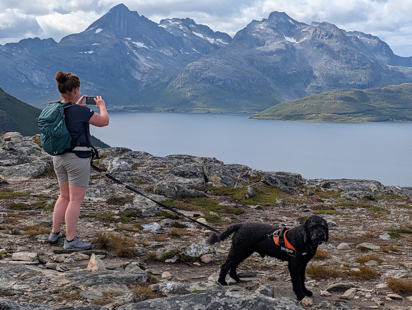 En mann med hund på en steinete kyst med fjell i bakgrunnen