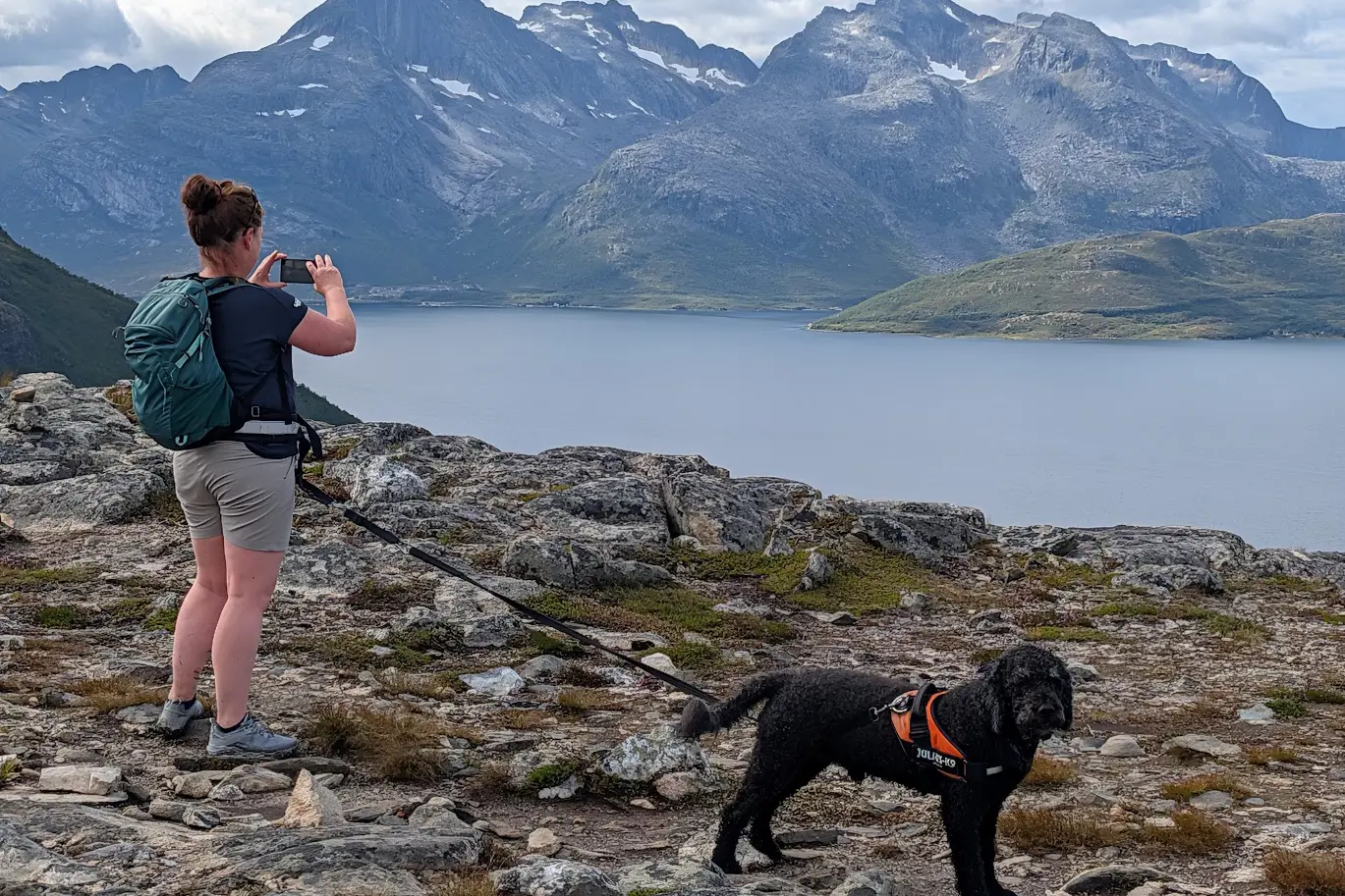 En mann med hund på en steinete kyst med fjell i bakgrunnen