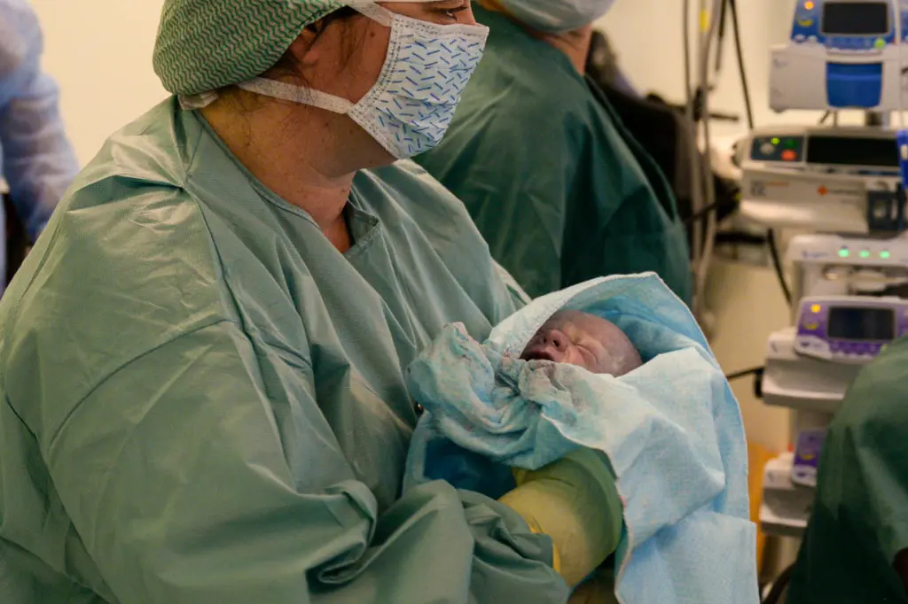 En person i kirurgisk skrubb som holder en baby