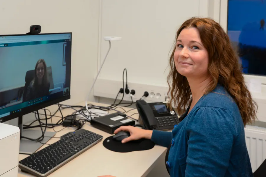 En person som sitter ved et skrivebord med en datamaskin og en telefon