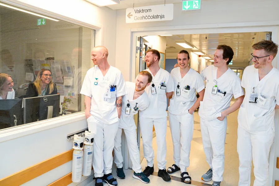 Seks mannlige ansatte kikker inn på vaktrom med to kvinner