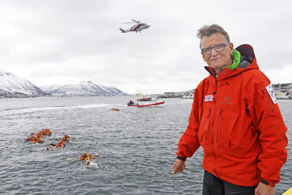 En mann som står foran en vannmasse med et helikopter som flyr over seg