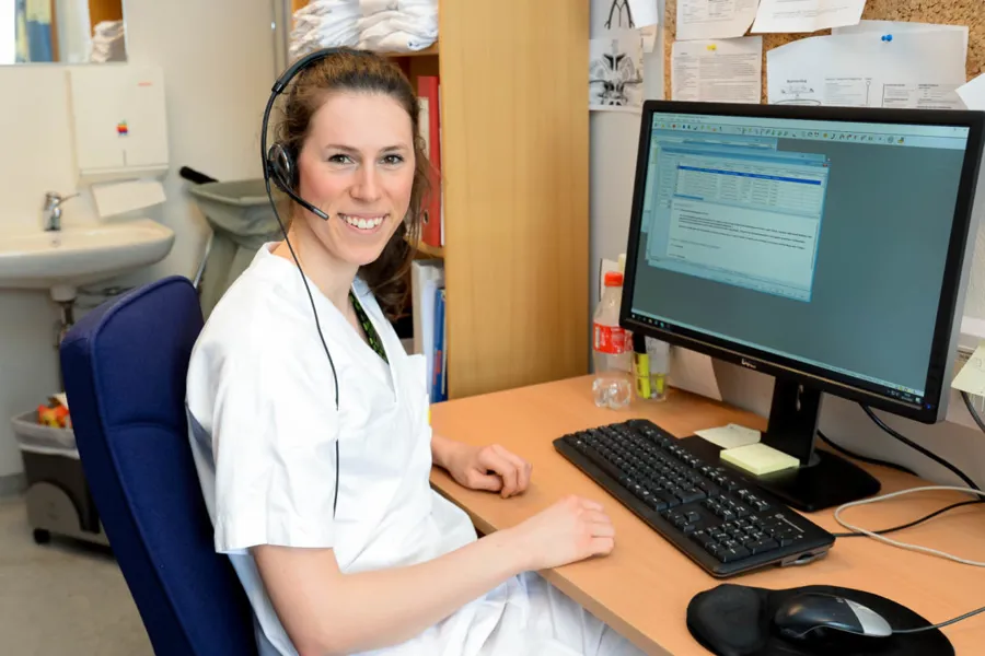 En person som har på seg et headset og sitter ved et skrivebord med en datamaskin