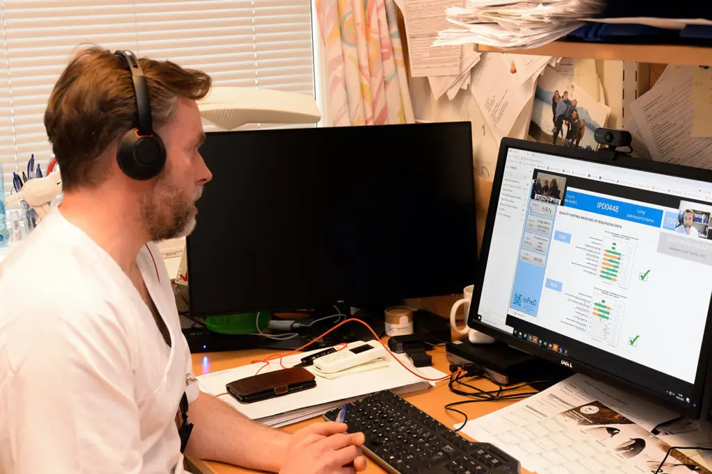 En mann med hodetelefoner og sitter ved et skrivebord med en datamaskin