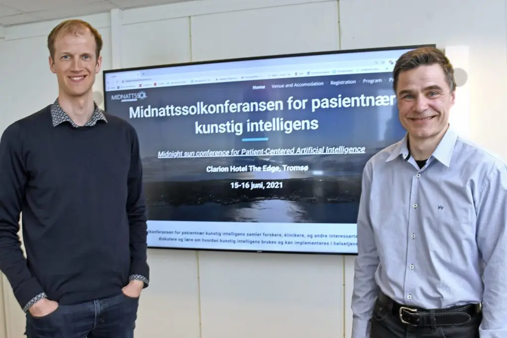 Et par menn som står foran en stor skjerm