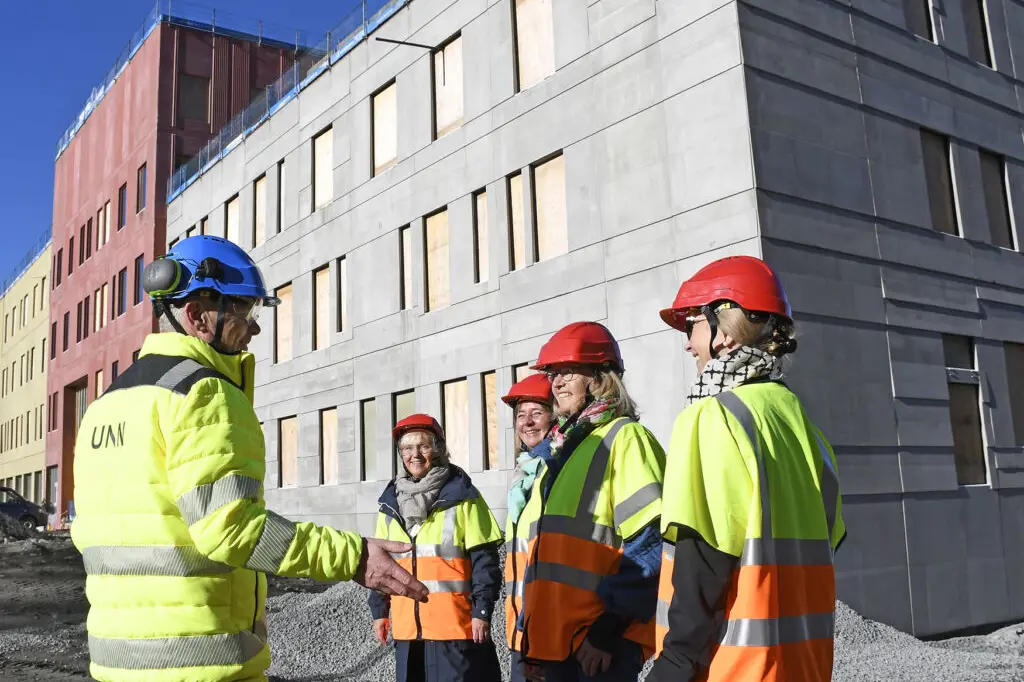 En gruppe menn i sikkerhetsvester som står utenfor en bygning