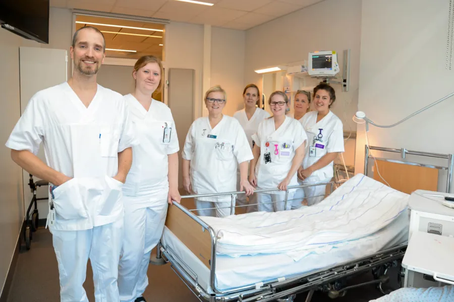 En gruppe mennesker i hvite laboratoriefrakker som står ved siden av en seng