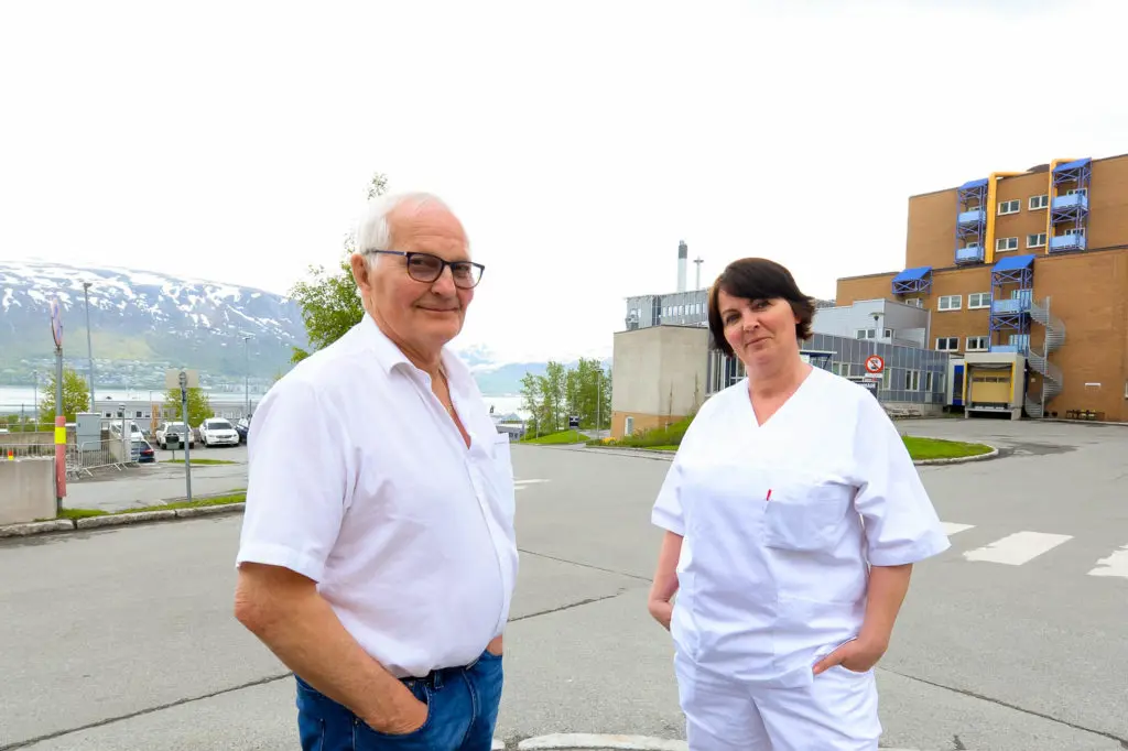 En mann og kvinne som står på en parkeringsplass med bygninger i bakgrunnen