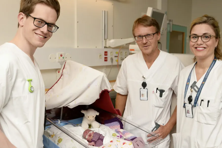 En gruppe mennesker i hvite skjorter som står ved siden av en baby i en sykehusseng