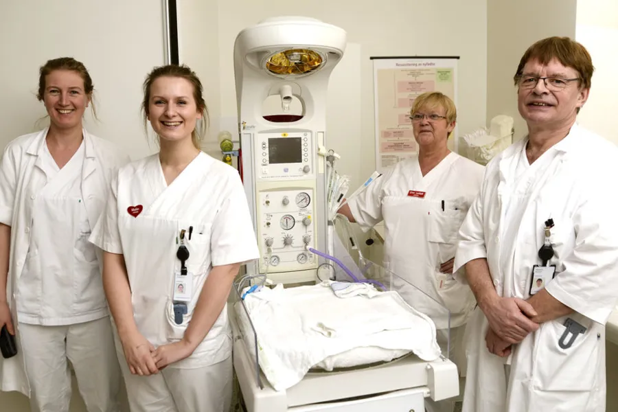 En gruppe mennesker i hvite laboratoriefrakker som står ved siden av en sykehusseng