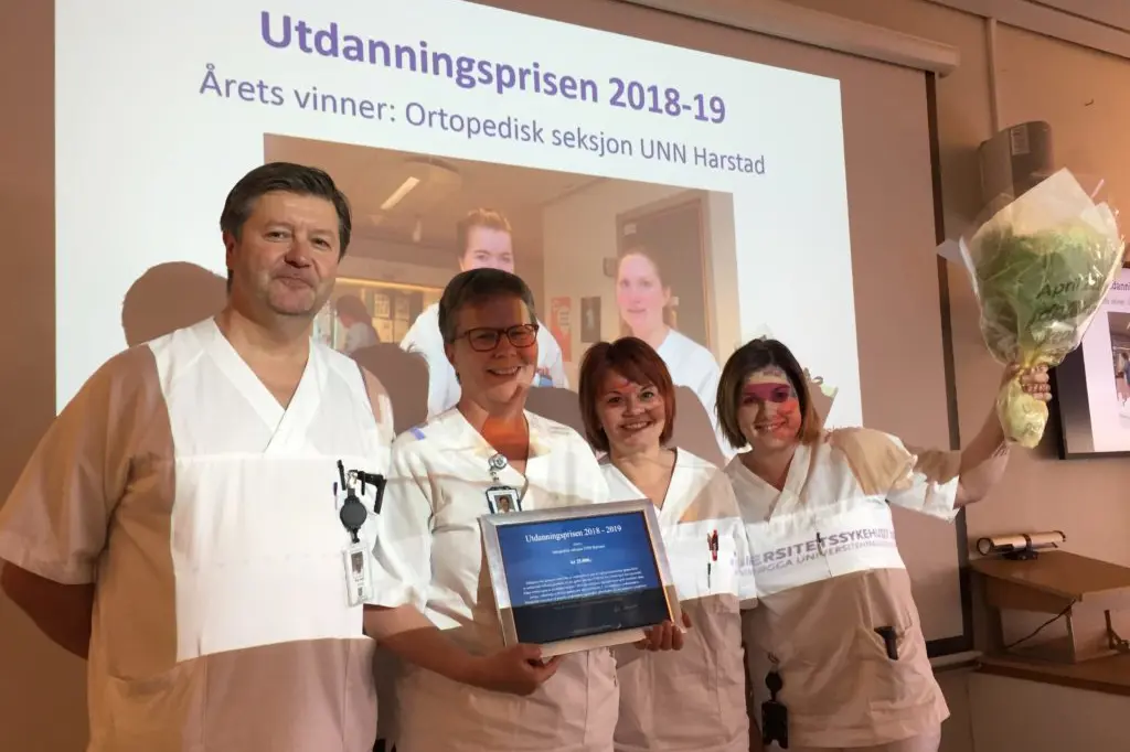 En gruppe mennesker i hvite laboratoriefrakker som holder en bærbar datamaskin