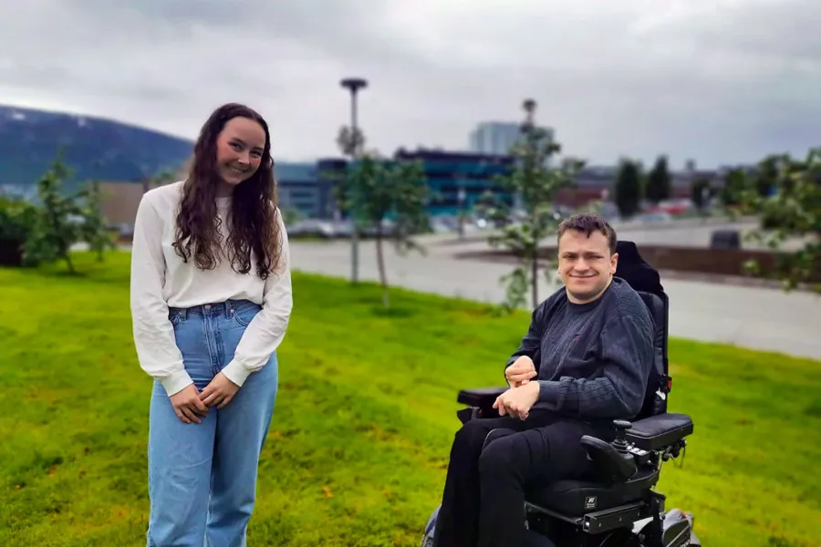 En mann og en kvinne som står ved siden av en rullestol i en park