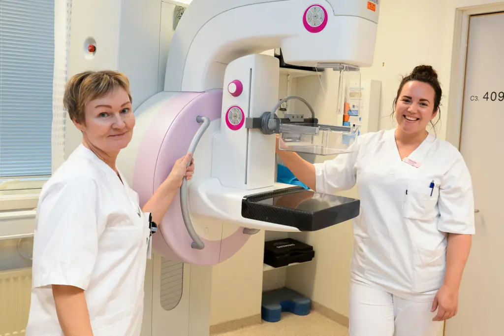 Et par kvinner i hvite laboratoriefrakker som står ved siden av en stor maskin