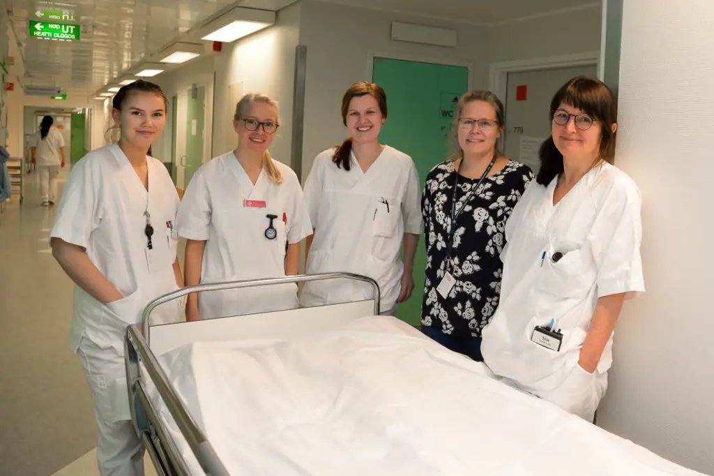 En gruppe kvinner i hvite laboratoriefrakker som står ved siden av en sykehusseng