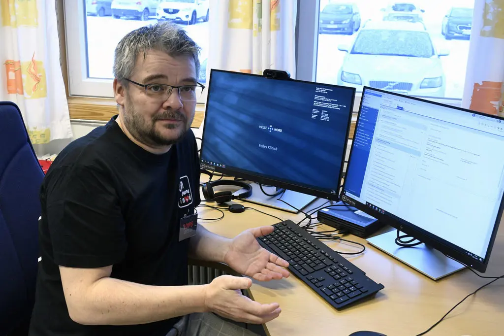 En mann som sitter ved et skrivebord med en datamaskin og et vindu