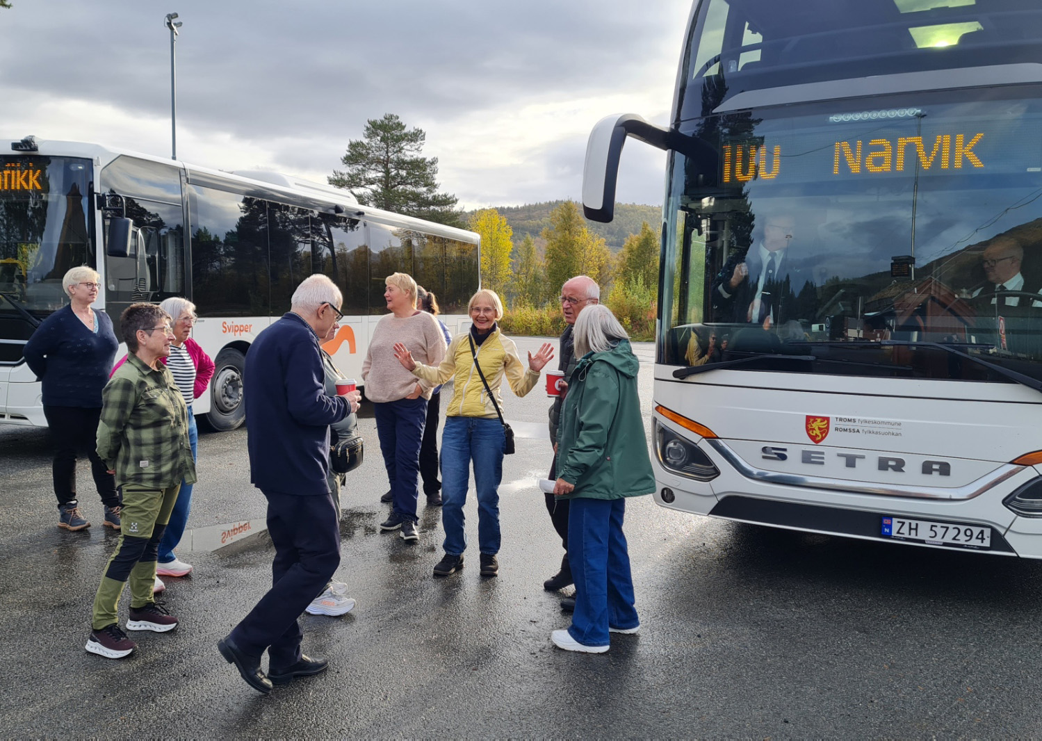 En gruppe mennesker som står ved siden av et par busser