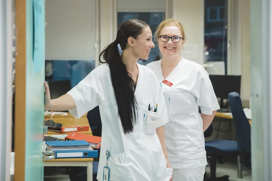 To ansatte i hvitt som står i ei døråpning