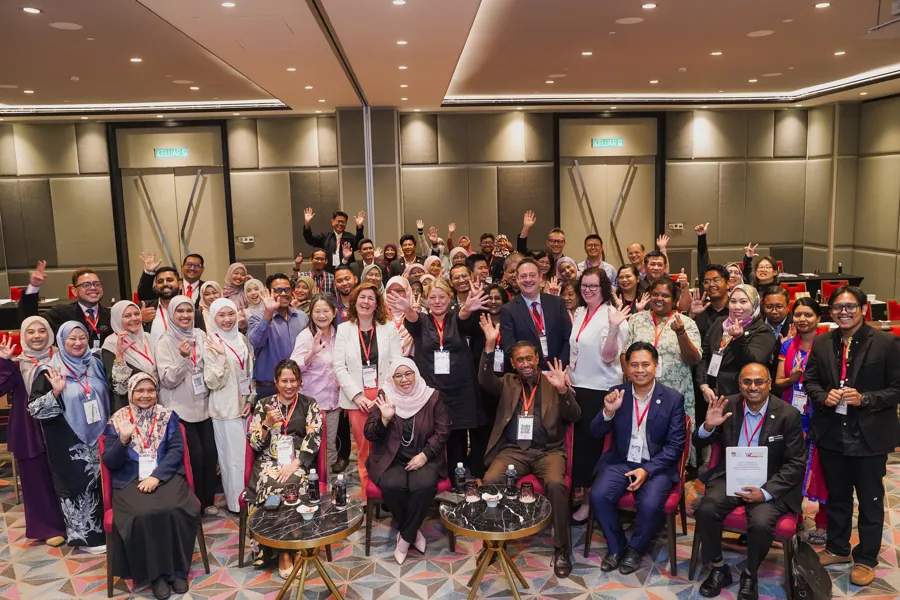 Stor gruppe mennesker samlet der alle ser inn i kameraet, noen vinker og andre gjør tegn med hendene.