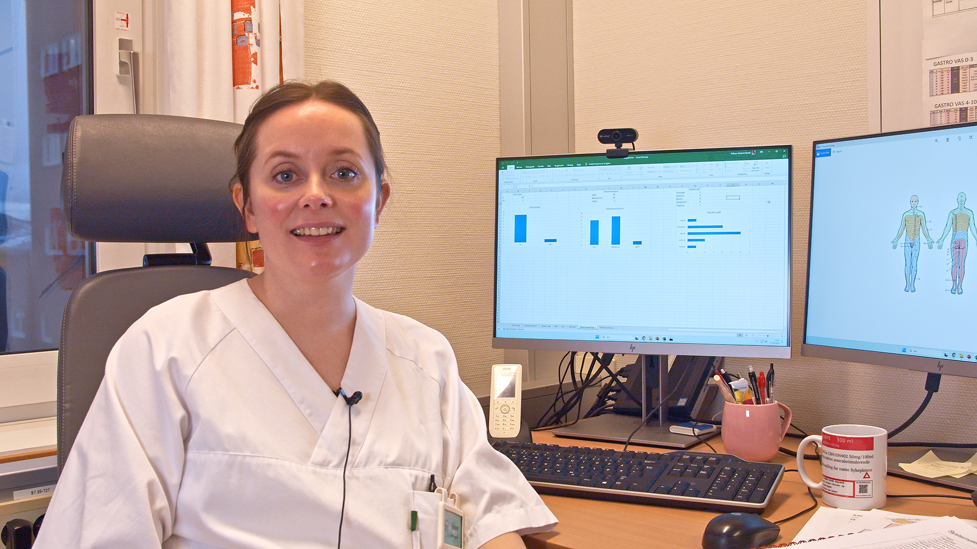 Hvitkledd ansatt som sitter forand arbeidsplassen med to PC skjermer